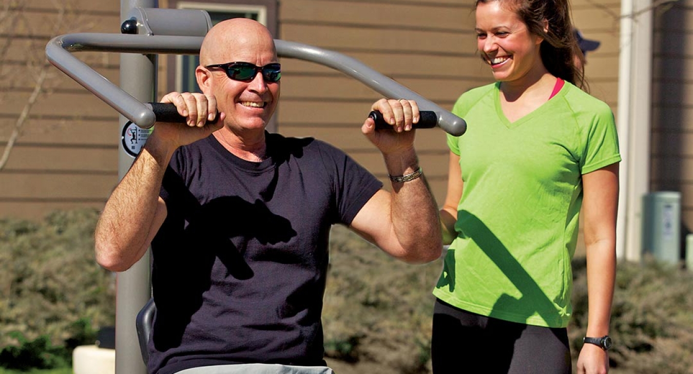 Couple doing shoulder presses on park fitness equipment