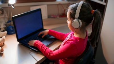 Little girl listening to music while studying on the computer