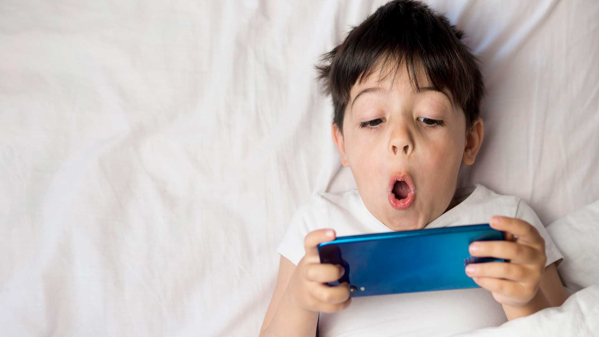 boy lying in bed on device