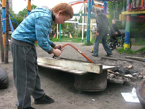 child sawing a post on adventure playground