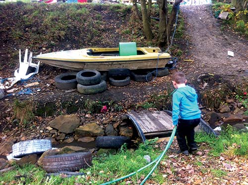 child with water hose crossing bridge to boat on dirt