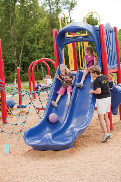 Girls sliding down slide with adult observing Girls sliding down slide with adult observing