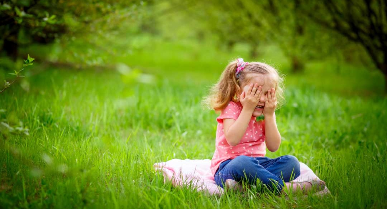 Young girl playing hid in seek in green grass