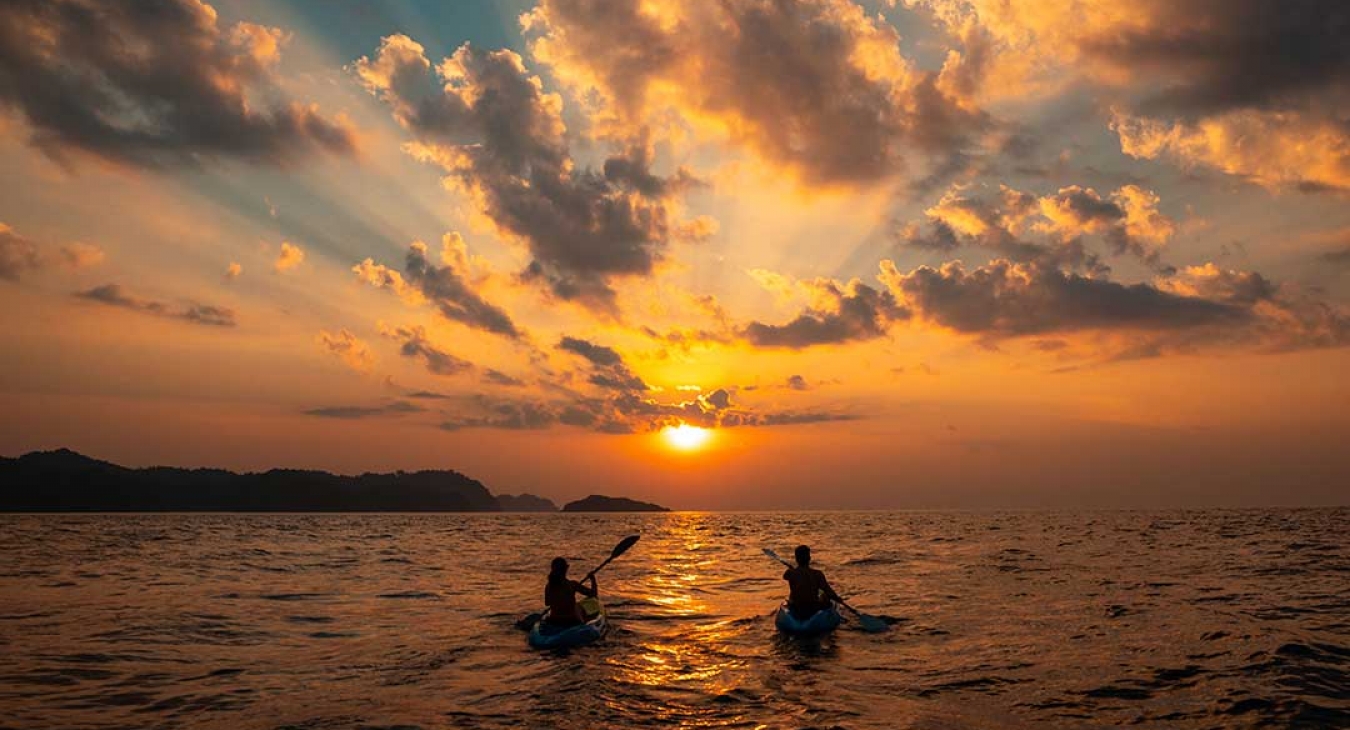 couple rowing kayaks into sunset