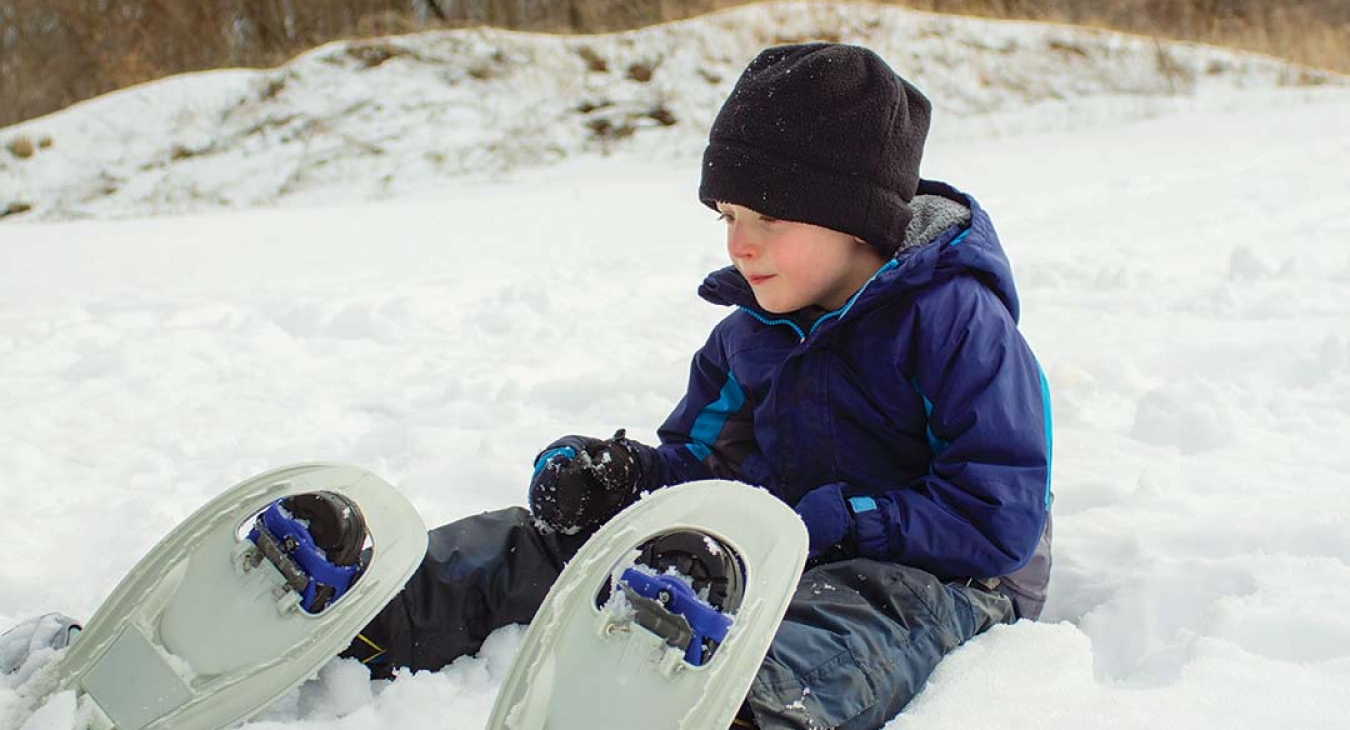 boy in snowshoes sitting in snow
